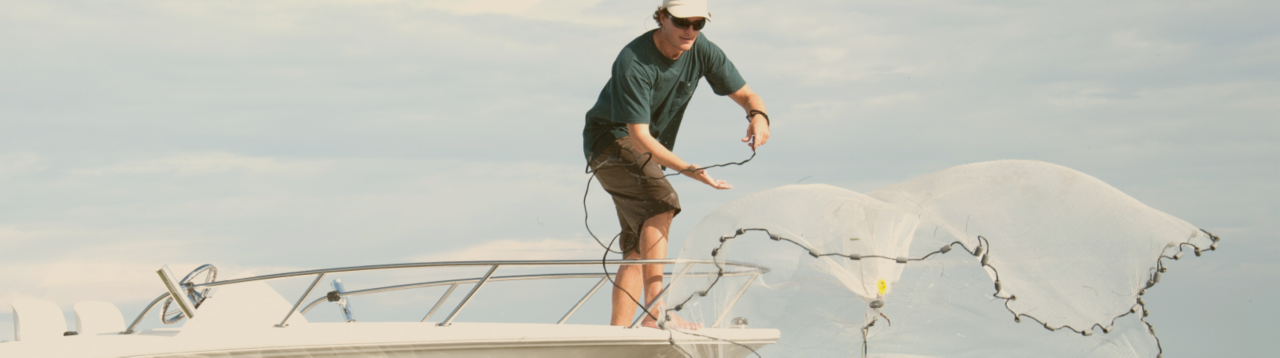 man casting net off a boateka boat